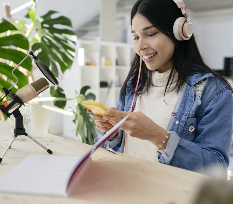 pretty latin hispanic woman doing a podcast with microphone notebook smartphone at home