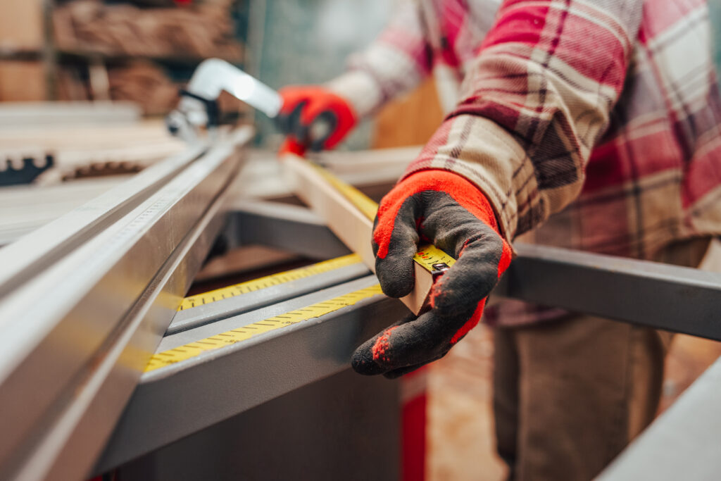 Worker in a carpentry shop measures plywood for cutting