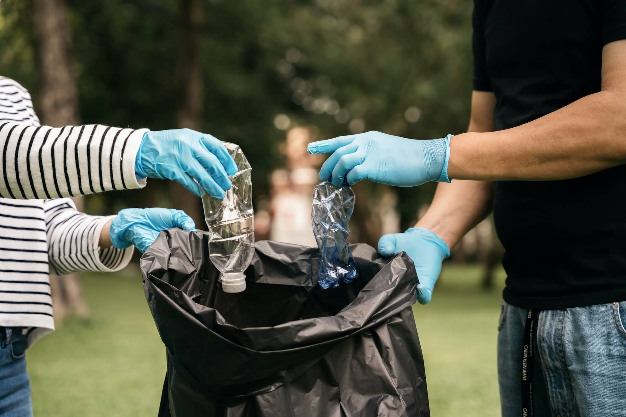 Hands of women and men collect plastic waste for cleaning at the park.